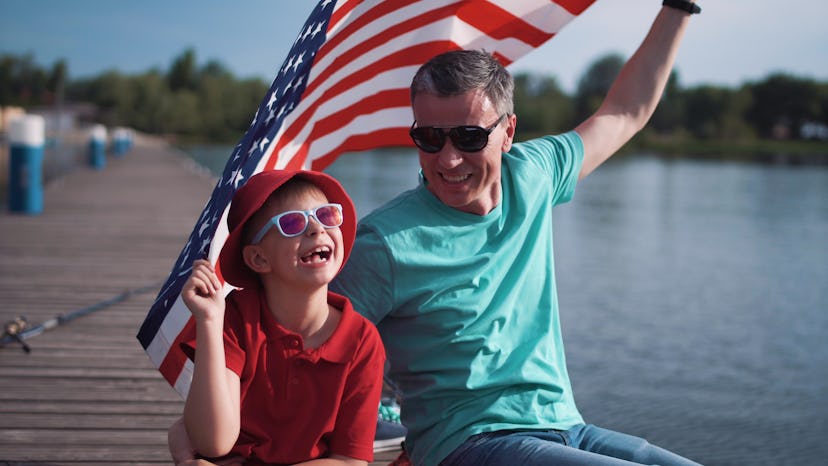 Father and son sitting on a dock, wearing sunglasses and holding the USA flag