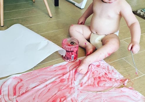 A little baby painting the floor with tempera paints