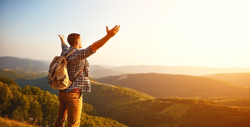 A man with a backpack spreading his arms while standing on a mountain