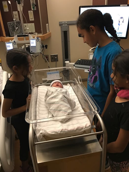 Three kids looking at a newborn baby in a hospital