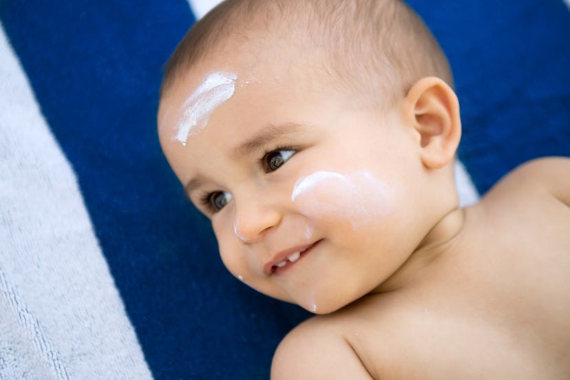 A baby lying on a towel with sunscreen on its face