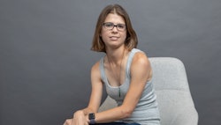 Jackie Noblett, who has Hypothalamic Amenorrhea, sitting in a grey top on a white chair