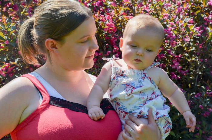 Risa Kerslake in a pink-black top holding her baby in a floral dress and looking at her