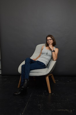 Jackie Noblett, posing in a grey top paired with jeans while sitting on a white chair
