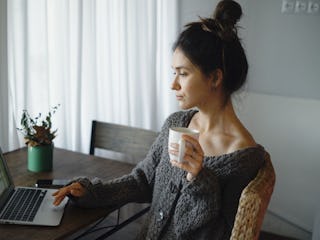 An anxious woman typing on her laptop and drinking tea