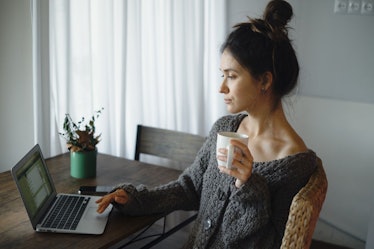 An anxious woman typing on her laptop and drinking tea