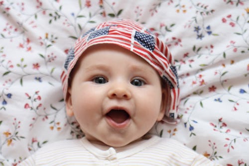 A baby lying on its back with an American flag print on its hat for July 4th