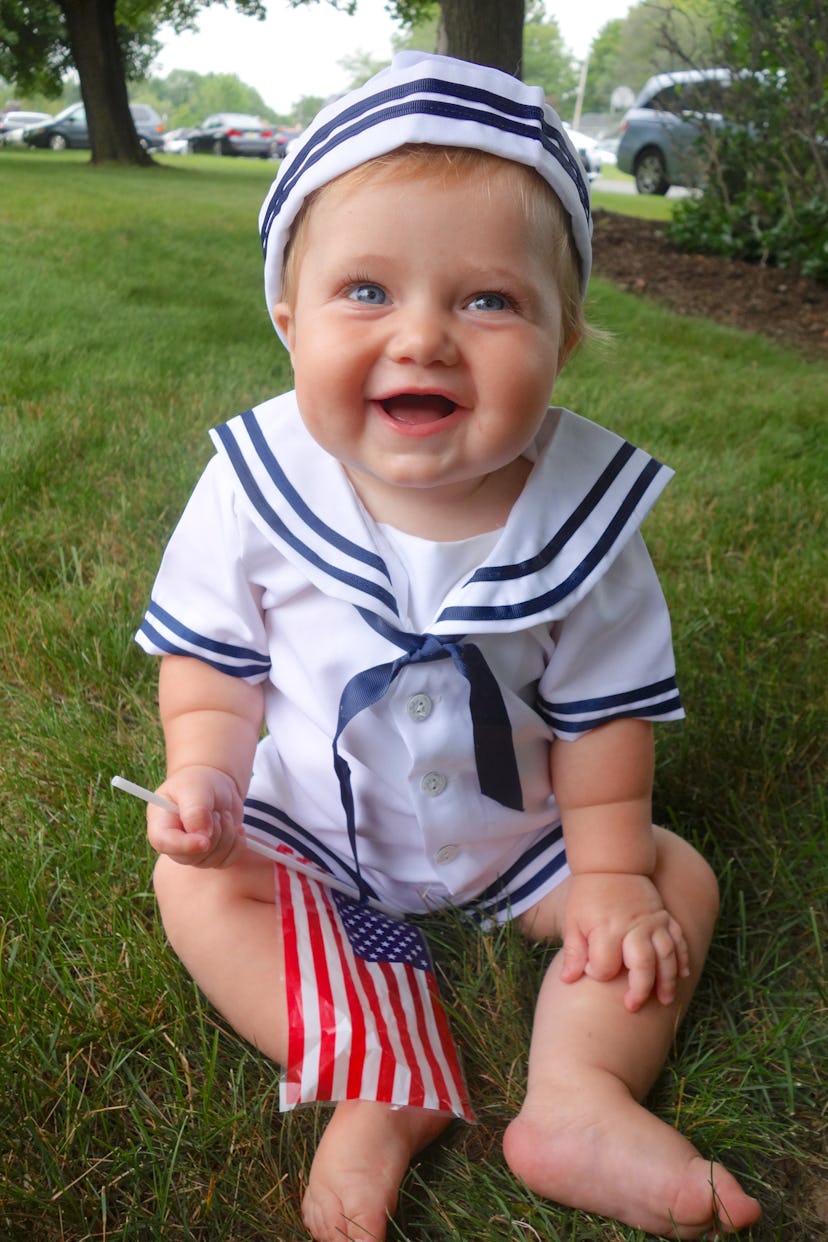 A baby holding the little American flag on the stick for the 4th of July, smiling for the picture