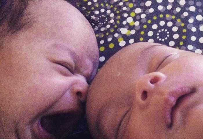 A closeup of twin babies, one is sleeping while the other is crying