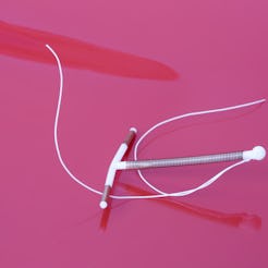 A white IUD on a pink background. OB-GYNs explain what you should know if you're getting an IUD.