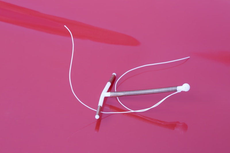 A white IUD on a pink background. OB-GYNs explain what you should know if you're getting an IUD.