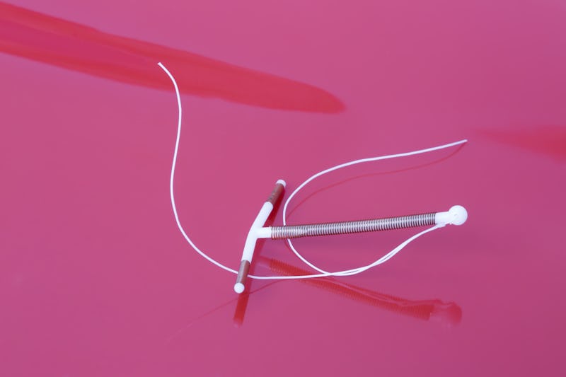 A white IUD on a pink background. OB-GYNs explain what you should know if you're getting an IUD.