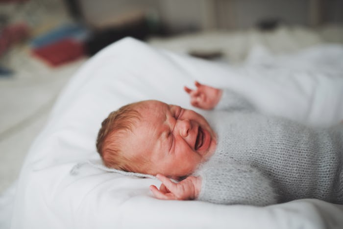 A newborn baby lying on its back on a pillow crying because of colic