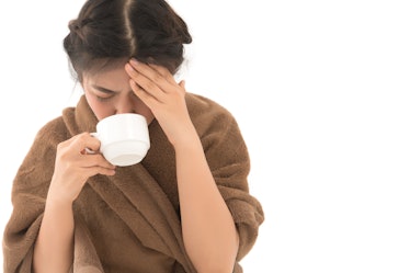 A girl with a headache holding a cup of tea.