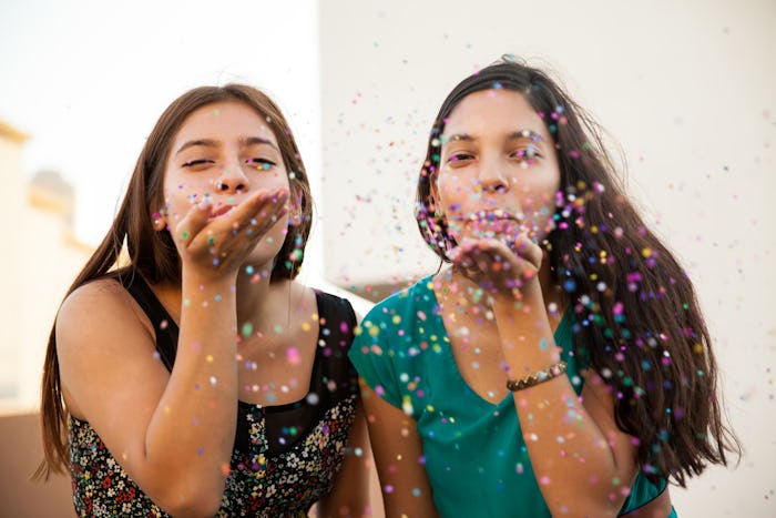Two friends blowing glitter from their palms while taking a photo for the National BFF Day.