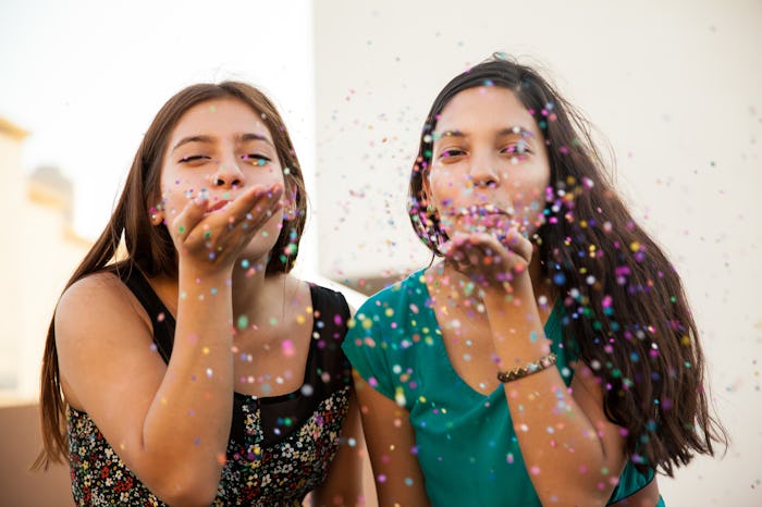 Two friends blowing glitter from their palms while taking a photo for the National BFF Day.