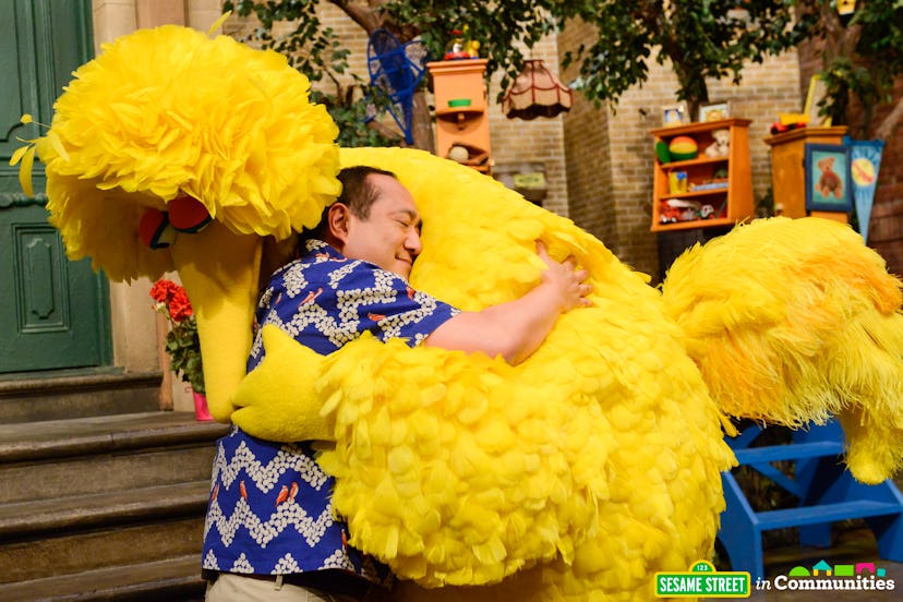 A man in a colorful shirt hugging a yellow bird from the Sesame workshop