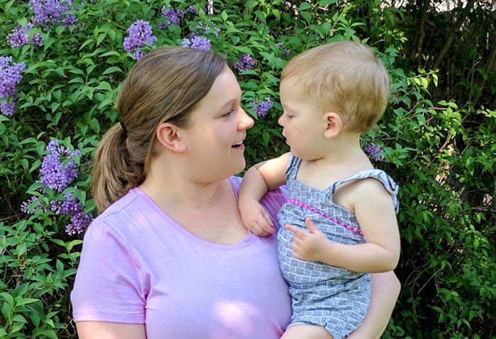 A woman holding her baby, both looking at each other and smiling with flowers in the background