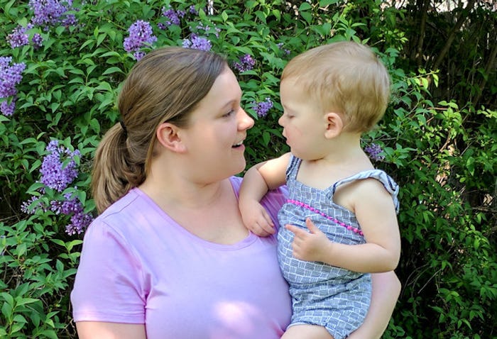 A woman holding her baby, both looking at each other and smiling with flowers in the background