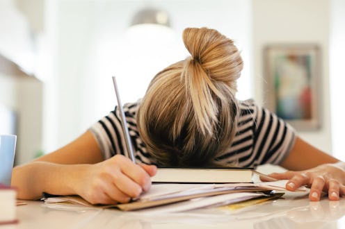 A woman with social anxiety puts her head on her notebook while holding a pen in her hand
