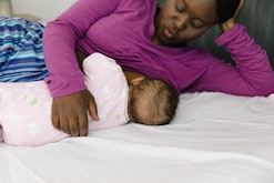Woman in purple shirt breastfeeding her baby on their bed
