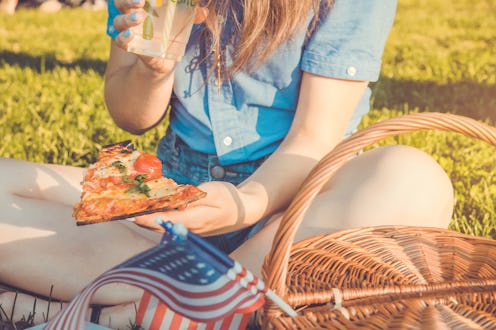 A woman sitting on the grass with her picnic basket next to her, eating pizza
