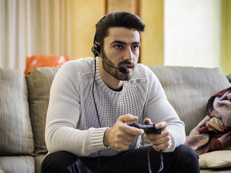 A man wearing a white sweater sitting on a couch with his headphones on while playing a video game