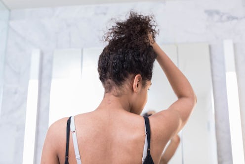 A woman holding her hair up while looking at herself in the mirror looking at areas that might be ST...