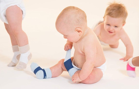 Baby boy pulling his sock from his feet while another baby is crawling towards him