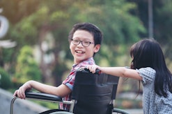 A girl pushign her brother in a wheelchair as he looks at the camera and smiles