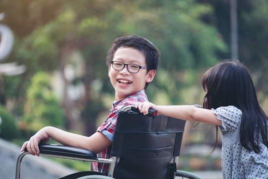 A girl pushign her brother in a wheelchair as he looks at the camera and smiles