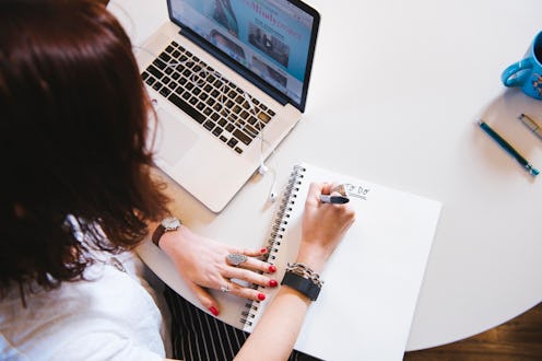 A woman looking at her laptop while writing in a notebook