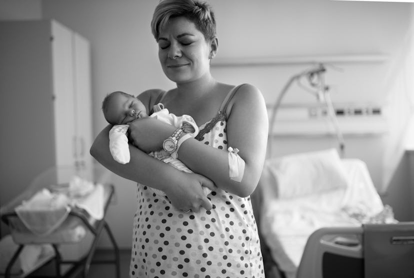 A woman in the hospital standing and holding her newborn 