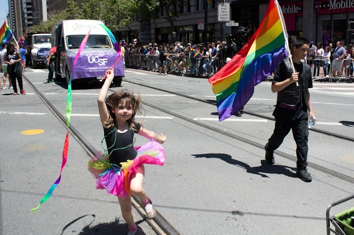 A man holding a flag and a little girl in a tutu skirt walking during a Pride event