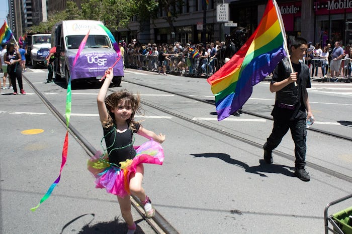 A man holding a flag and a little girl in a tutu skirt walking during a Pride event