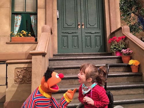 Bert from sesame street standing in front of a flight of steps with a child in a wheelchair