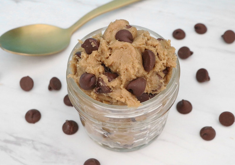 Cookie dough served in a small jar with a spoon and chocolate chips over the table