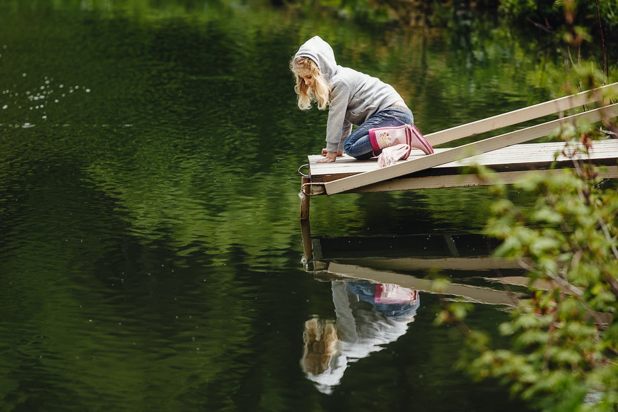 A blonde girl sitting on the edge of a lake wooden dock