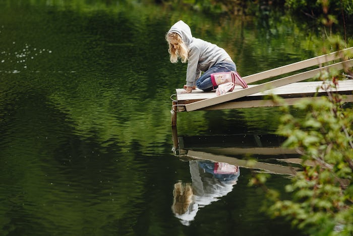 A blonde girl sitting on the edge of a lake wooden dock