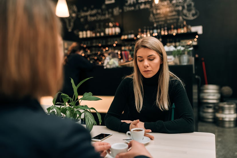 Two women talking over coffee. One woman looks at the table, clearly upset. 