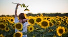 Young woman dancing in a field of sunflowers before posting a pic on Instagram with flower captions.