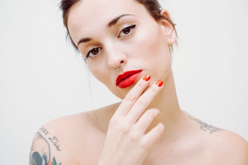 A woman with red false nails, a tattoo on her shoulder, her hair in an updo wearing a red lipstick