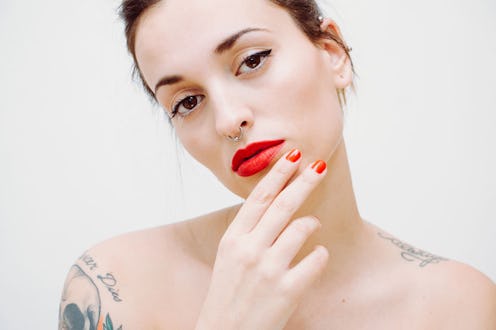 A woman with red false nails, a tattoo on her shoulder, her hair in an updo wearing a red lipstick 