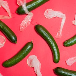 Six cucumbers with used condoms next to each on a pink surface.
