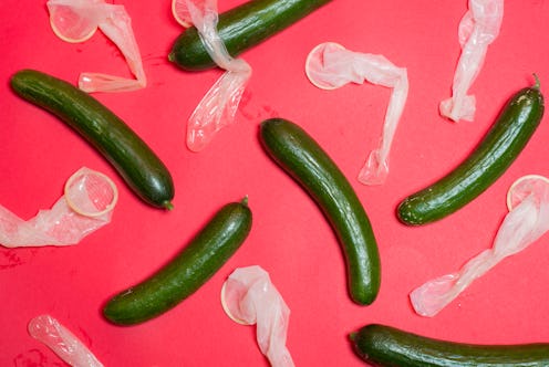 Six cucumbers with used condoms next to each on a pink surface.