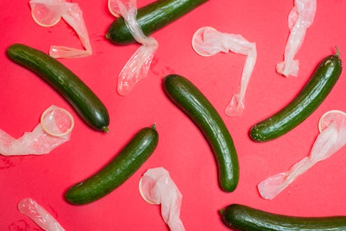 Six cucumbers with used condoms next to each on a pink surface.