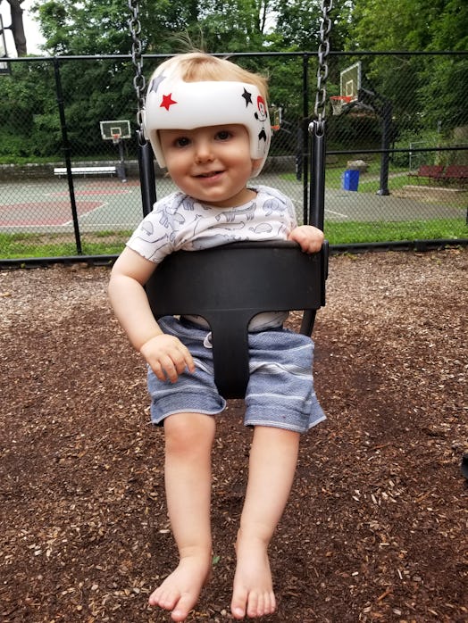 A baby boy sitting in a swing while wearing a white helmet
