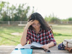 A college student studying while holding her head because of migraine pain