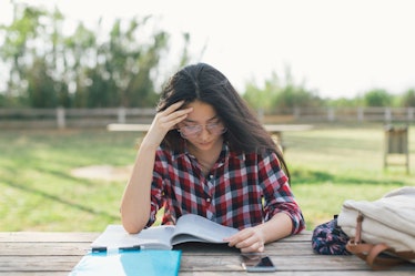 A college student studying while holding her head because of migraine pain