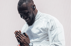 Stormzy wearing a white Adidas jacket and holding a mic